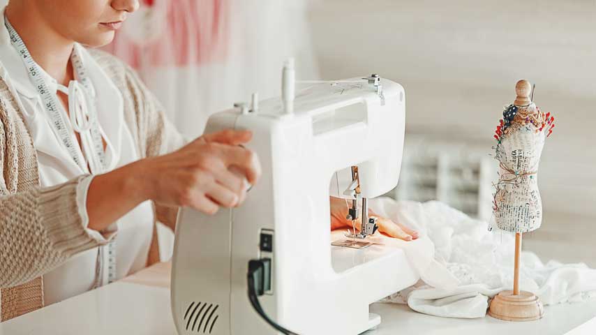Mulher branca mechendo no volante da máquina de costura.