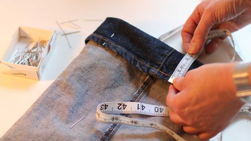 Uma pessoa tirando medida de uma barra de calça para realizar ajustes e reparos